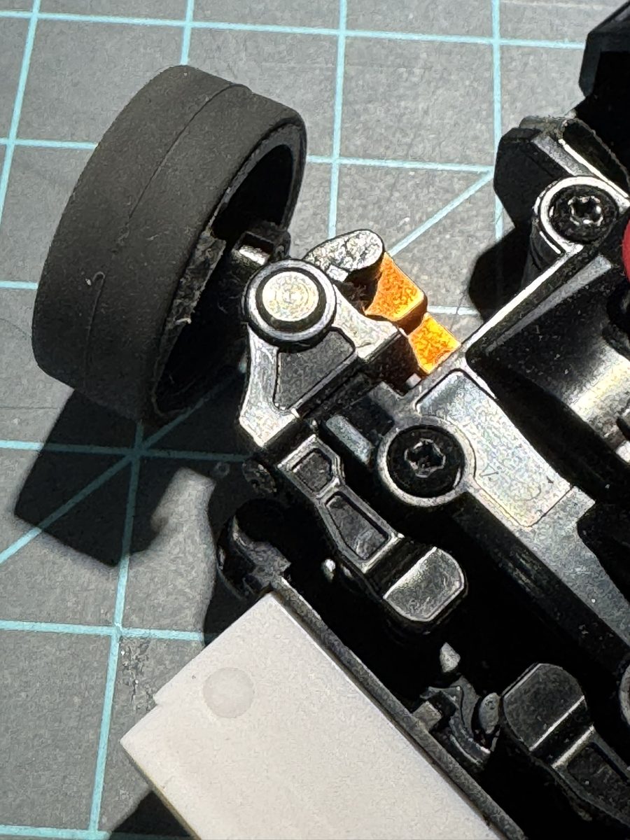 MR-03 front suspension after king pin flip. Orange clip now visible at the lower knuckle, ball end seated up in the knuckle, pin tail trimmed flush; top-down view showing flipped orientation