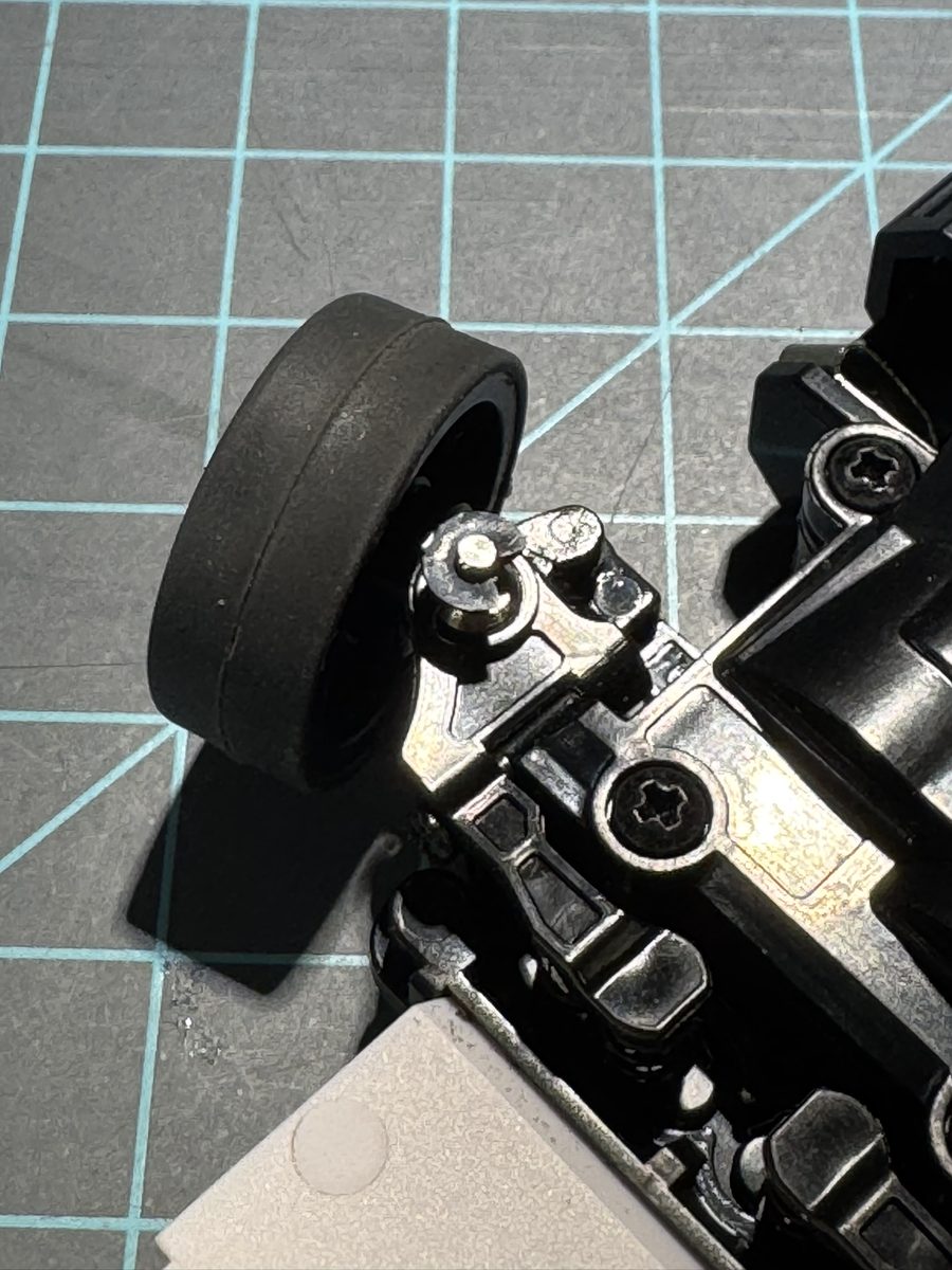 MR-03 front suspension in stock orientation, clip visible at the top of the steering knuckle, pin shaft descending through the knuckle bore; top-down view over the front-right corner
